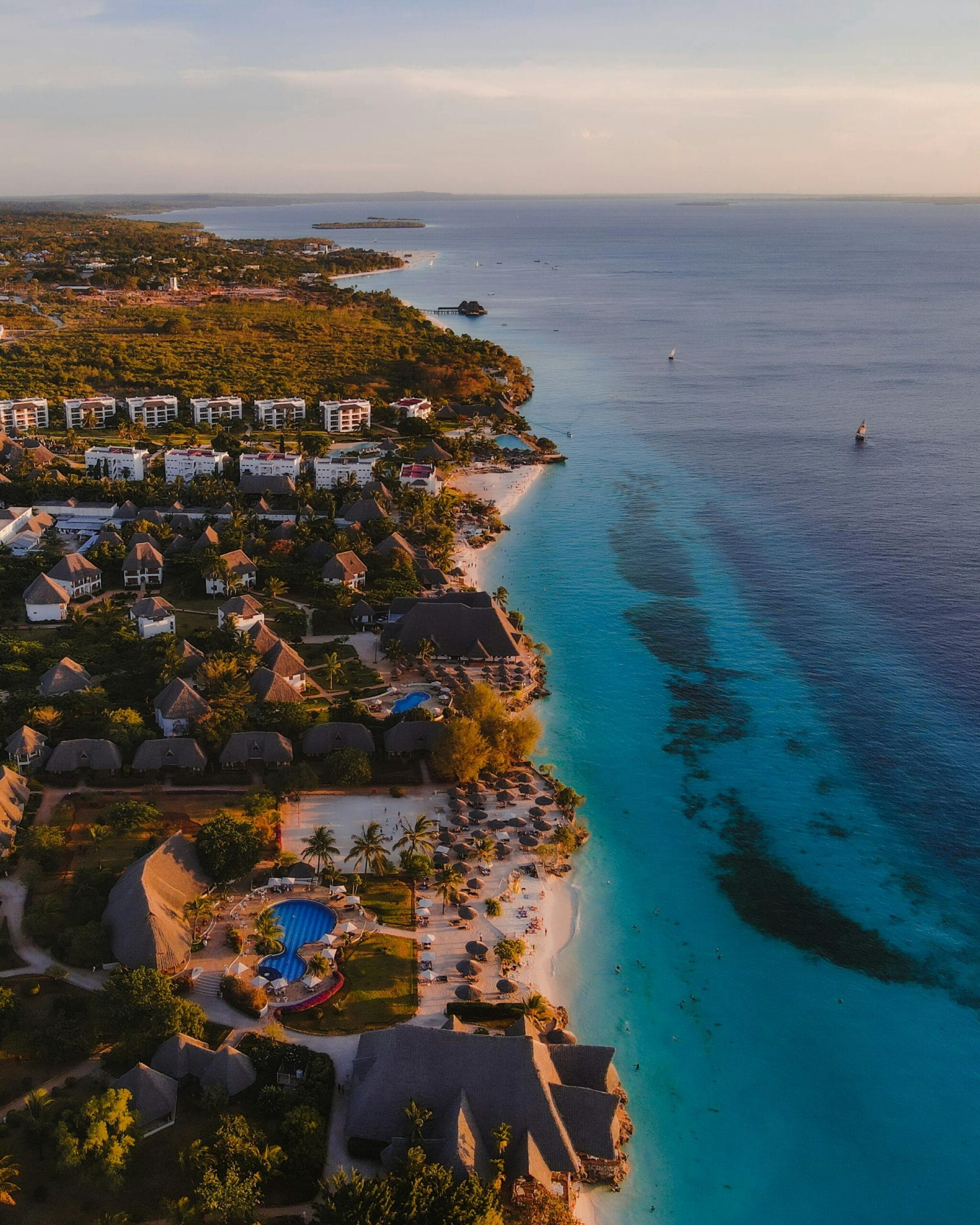 Best family resorts in Zanzibar 1 Stunning aerial view of Zanzibar's shoreline with resorts, lush nature, and vibrant ocean hues during sunset.