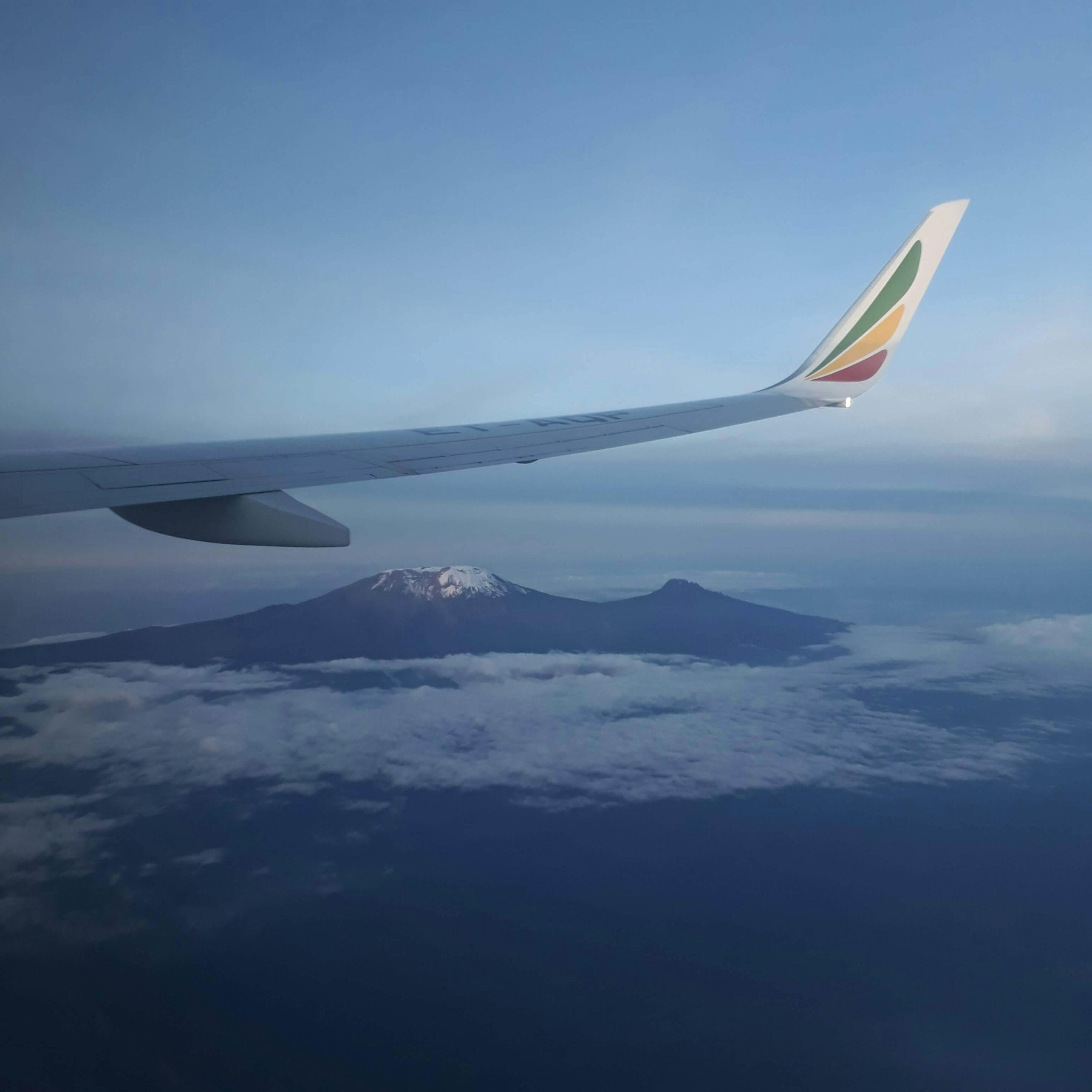 Airplane wing view over Mount Kilimanjaro and clouds during flight.