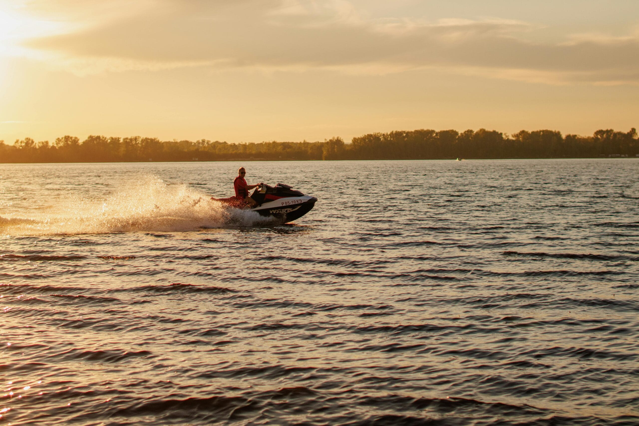 Zanzibar Jet Ski Adventure: Ultimate Ocean Thrill & Coastal Exploration Experience 1 A jet ski speeds across a lake at sunset, with water splashing behind.